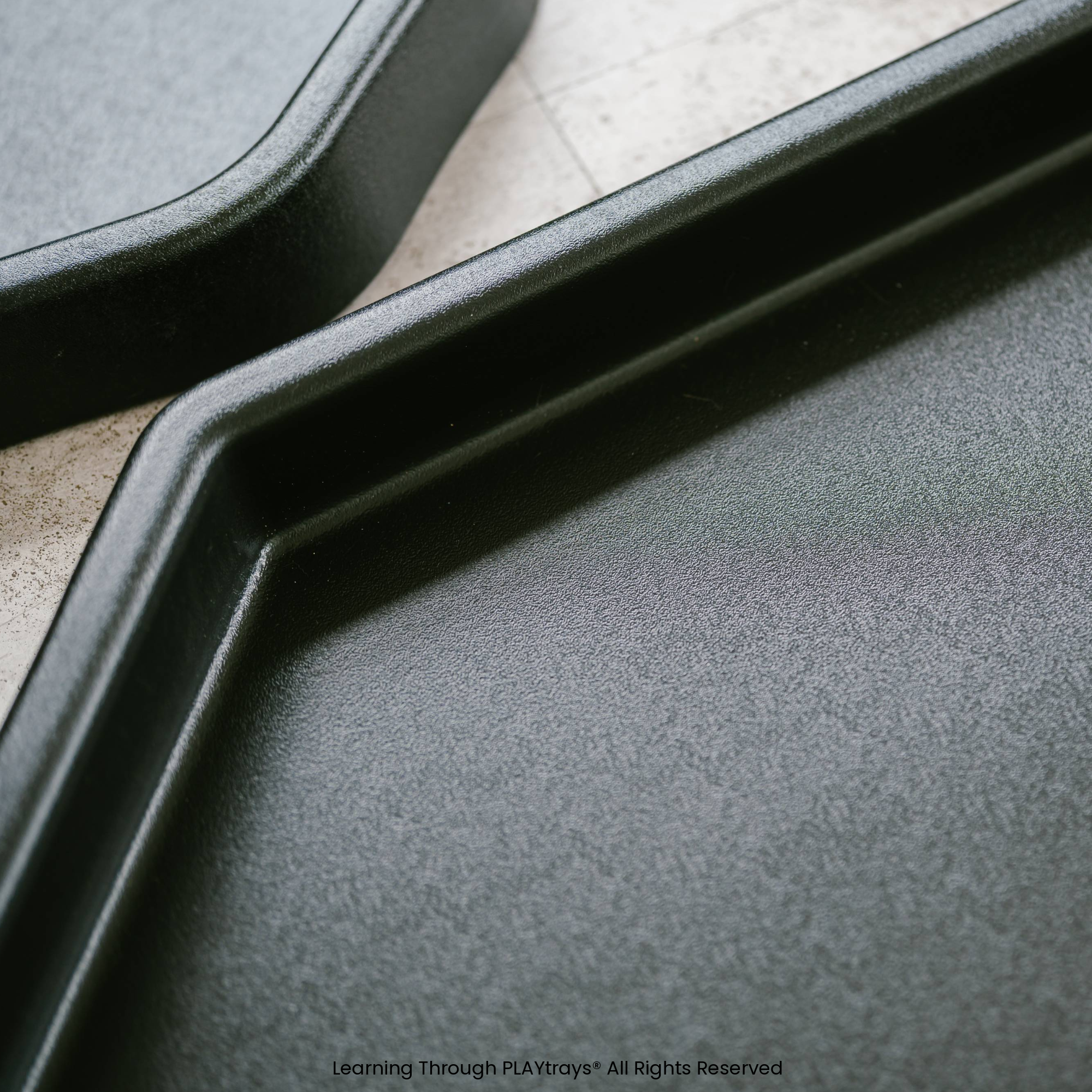 Close-up of a black tray with a textured surface on a concrete floor.