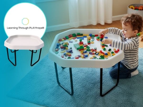 Child playing with colorful building blocks on a white play table with a chair.